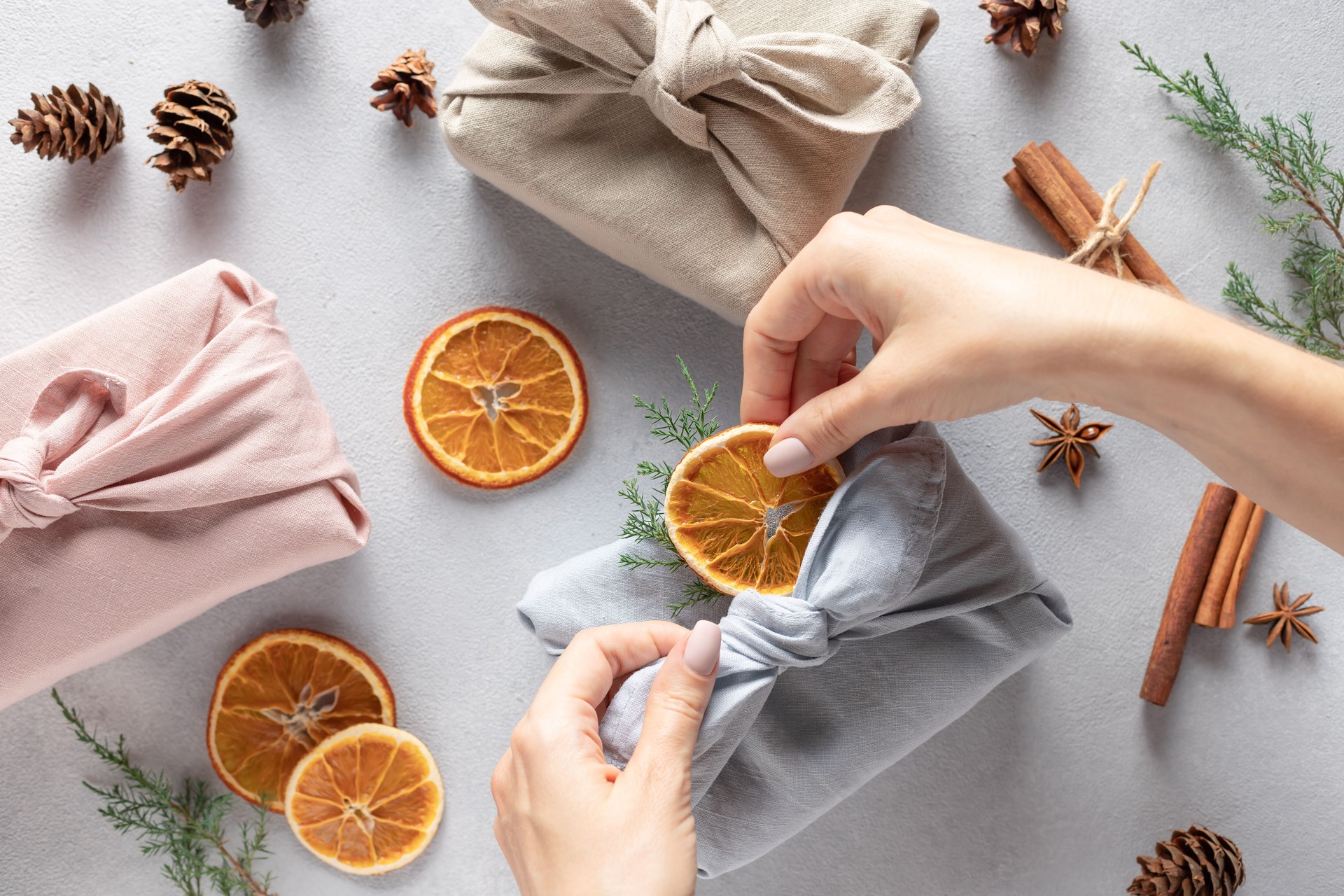 female hands packing gifts in linen cloth. Furoshiki gifts